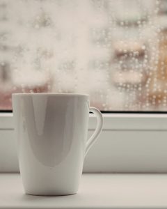 A white mug resting on a windowsill beside rain-covered glass, creating a quiet and reflective atmosphere that represents grief, support, and moments of emotional pause.